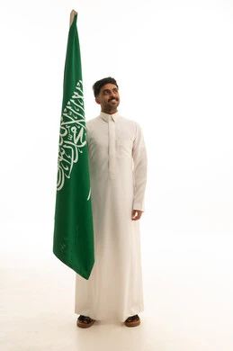 رجل سعودي بالثوب التقليدي مع علم المملكة