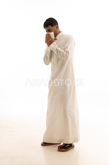 رجل سعودي يرتدي الثوب الأبيض يعطس في منديل ورقي
