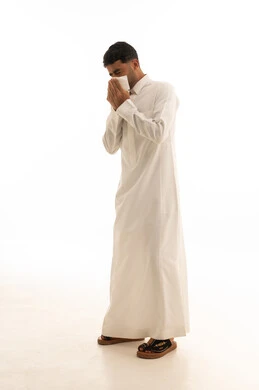 رجل سعودي يرتدي الثوب الأبيض يعطس في منديل ورقي