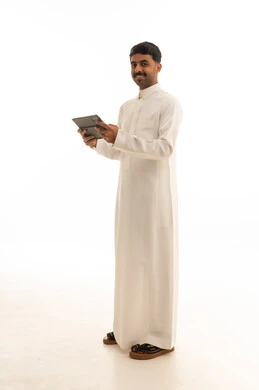 رجل سعودي بالثوب التقليدي يحمل جهاز لوحي بخلفية بيضاء