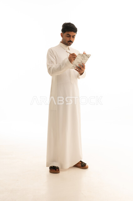 رجل سعودي بالثوب الأبيض يكتب على لوحة ملاحظات
