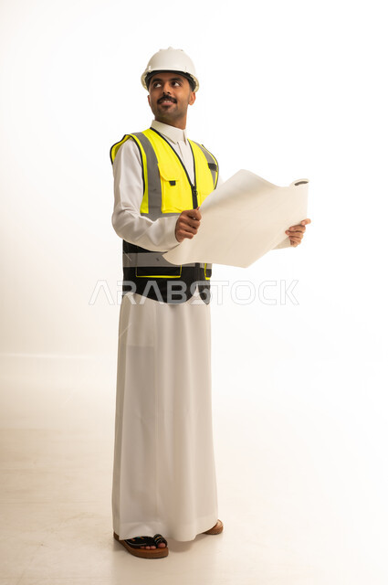 مهندس سعودي بالثوب التقليدي يحمل مخطط بناء معماريا