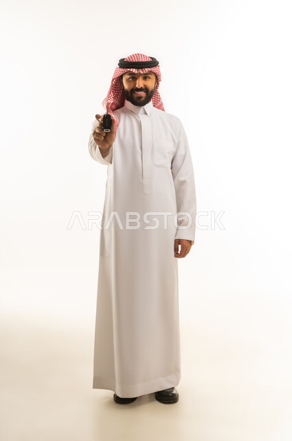 رجل سعودي بالزي التقليدي يمسك مفتاح سيارة بخلفية بيضاء