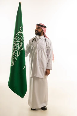 طبيب سعودي بالزي التقليدي مع علم المملكة العربية السعودية