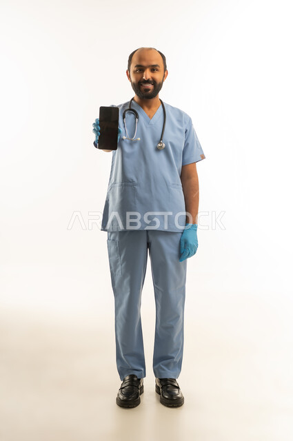 Saudi Male Doctor Holding Smartphone in Blue Scrubs