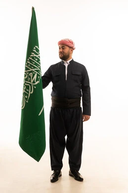 رجل بالزي الكردي التقليدي يحمل علم المملكة العربية السعودية
