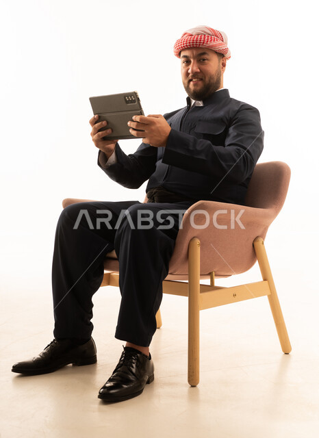 رجل بالزي الكردي التقليدي مع جهاز لوحي على كرسي وردي