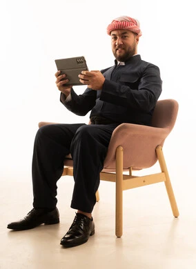 رجل بالزي الكردي التقليدي مع جهاز لوحي على كرسي وردي