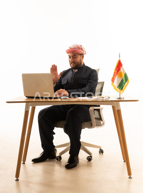 رجل بالزي الكوردي التقليدي يستخدم المحمول على المكتب