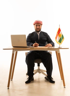 رجل كردي بالزي التقليدي يجلس خلف مكتب عمل