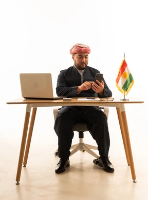 Kurdish Man at Desk with Smartphone and Laptop