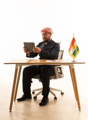 رجل كردي بالزي التقليدي يستخدم جهاز لوحي خلف المكتب