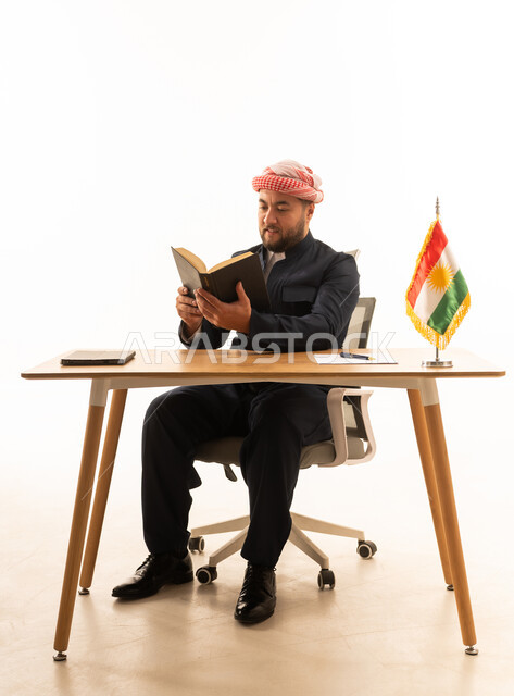 رجل بالزي الكردي يقرأ كتاباً خلف مكتبه
