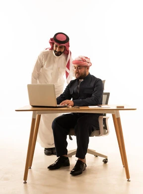 رجل سعودي وكوردستاني يعملان على لابتوب بخلفية بيضاء