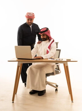 رجل سعودي وكردي يعملان على حاسوب محمول بخلفية بيضاء