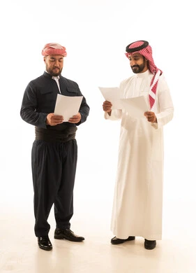 رجل سعودي وكردي يراجعان وثائق ورقية على خلفية بيضاء
