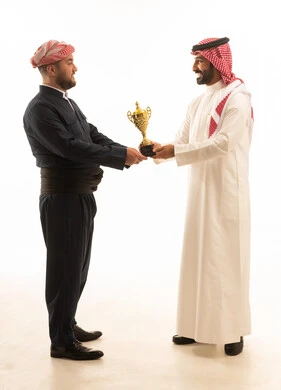رجل سعودي وكوردي يحملان كأساً ذهبياً بخلفية بيضاء
