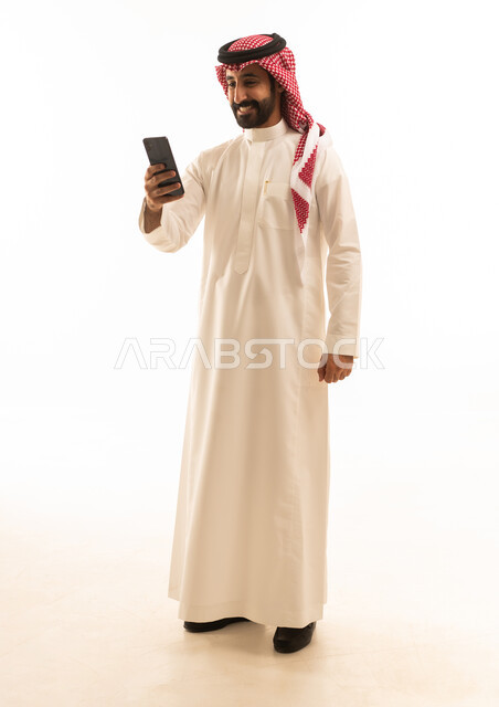 رجل سعودي بالثوب يستخدم الهاتف الذكي بخلفية بيضاء