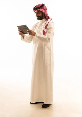رجل سعودي بالثوب الأبيض يستخدم جهازاً لوحياً خلفية بيضاء