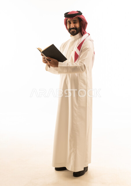 رجل سعودي بالزي التقليدي يمسك كتاباً