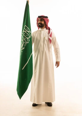 رجل سعودي يحمل العلم الوطني على خلفية بيضاء