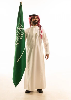 رجل سعودي بالثوب التقليدي يحمل علم المملكة العربية السعودية