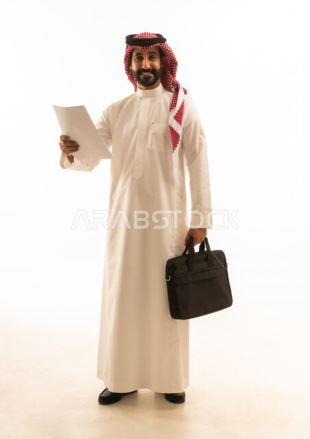 رجل أعمال سعودي بالزي التقليدي يحمل أوراقاً وحقيبة عمل