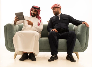 رجل سعودي وكوردستاني يستخدمان جهاز لوحي على الأريكة