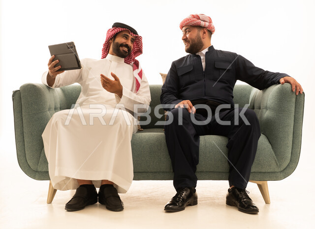 رجل سعودي وكردي مع جهاز لوحي على أريكة