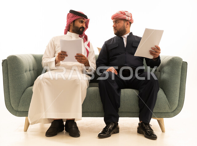 رجل سعودي وكوردستاني يراجعان مستندات على أريكة خضراء