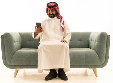 رجل سعودي يستخدم الهاتف الذكي على أريكة خضراء