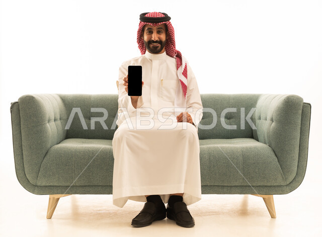 Saudi Man Sitting on Sofa Holding Smartphone White Background