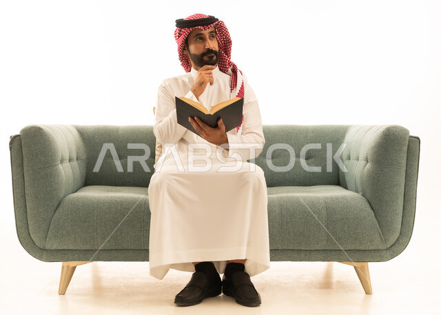 رجل سعودي يقرأ كتاباً على الأريكة بخلفية بيضاء