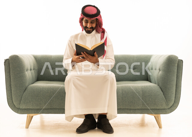 رجل سعودي باللباس التقليدي يقرأ كتاباً على أريكة خضراء