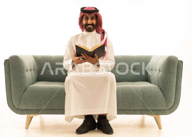 Saudi Man in Thobe Reading Book on Grey Sofa