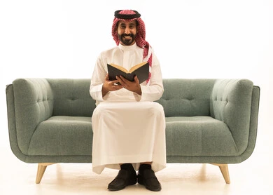 رجل سعودي بالزي التقليدي يقرأ كتاباً على أريكة