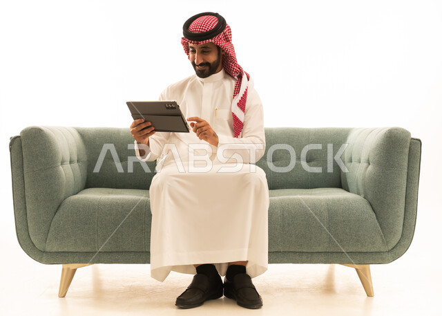 رجل سعودي يستخدم جهاز لوحي على أريكة خضراء في استوديو