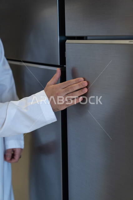 رجل سعودي بالثوب يلمس ثلاجة حديثة