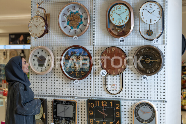 Saudi Woman Browsing Decorative Wall Clocks in Store