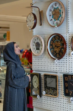 امرأة سعودية بالعباءة تتسوق لشراء ساعات الحائط