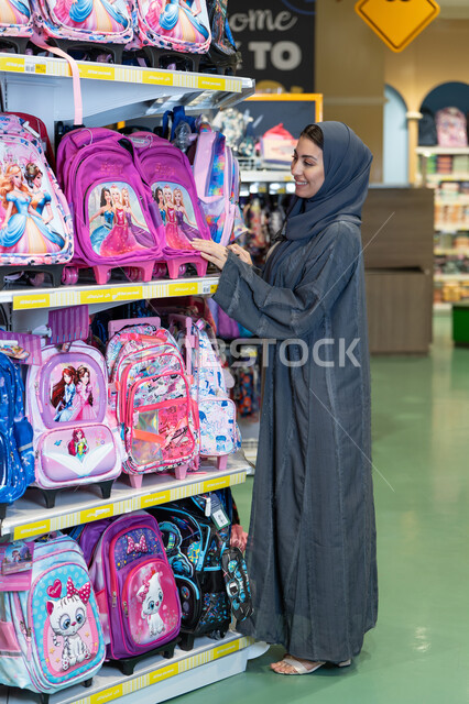 امرأة عربية بالعباءة تتسوق لشراء الحقائب المدرسية