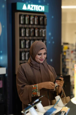 امرأة إماراتية تستخدم الهاتف في متجر إلكترونيات