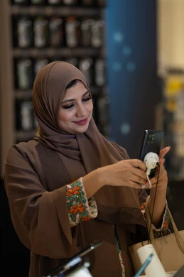 امرأة عربية تختبر هاتفاً ذكياً في متجر إلكترونيات