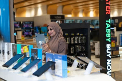 امرأة سعودية تتفحص جهازاً لوحياً داخل متجر إلكترونيات حديث