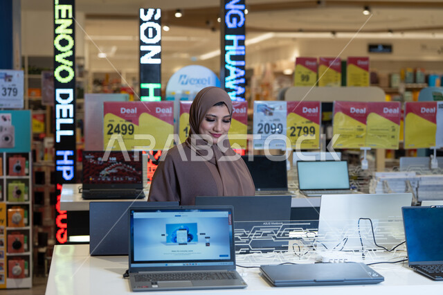 امرأة عربية تتسوق لشراء لابتوب في متجر إلكترونيات
