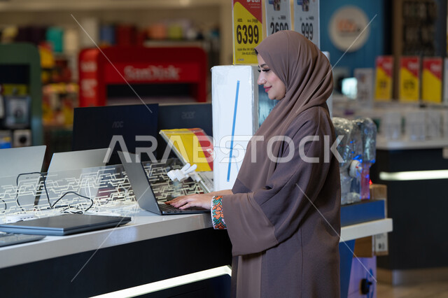امرأة إماراتية تجرب جهاز لابتوب في متجر إلكترونيات