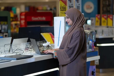 امرأة إماراتية تجرب جهاز لابتوب في متجر إلكترونيات