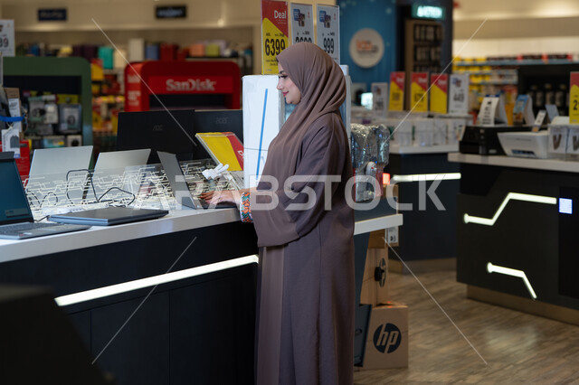 امرأة عربية بالعباءة تستخدم لابتوب في متجر إلكترونيات