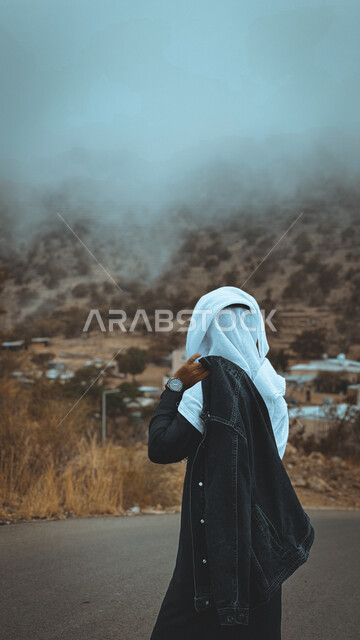 زاوية من الخلف لرجل خليجي سعودي ينظر لجمال مدينة الطائف بالمملكة العربية السعودية في فصل الشتاء ، أماكن سياحية في السعودية ، جو ضبابي على جبال الطائف ، المرتفعات الجبلية 