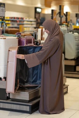 امرأة عربية بعباءة تتسوق لشراء حقيبة سفر في متجر